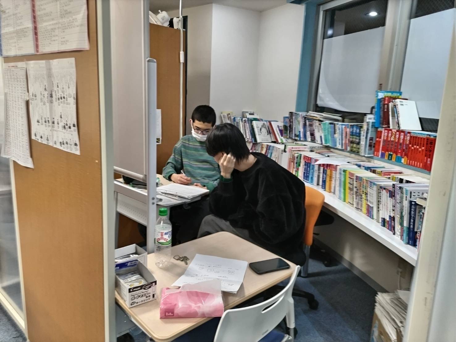 教室の本棚のそばで、隣り合って教材に向き合う授業風景